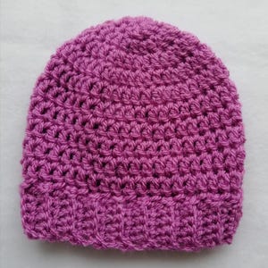 May include: A handmade, magenta-colored crochet beanie hat. The hat features a textured stitch pattern throughout the crown and a ribbed brim. This warm hat is perfect for cold weather and is a stylish accessory.