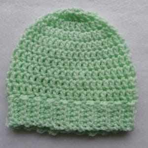 May include: A light green, handmade crochet beanie hat. The hat is made with a textured stitch pattern and features a ribbed brim. The soft, pastel color and handmade quality suggest it is for a baby or child.