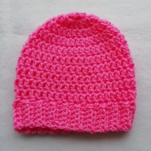 May include: A bright pink, handmade crochet beanie hat. The hat is made with a textured stitch and features a ribbed brim. The hat is a solid color and appears to be made of soft yarn.
