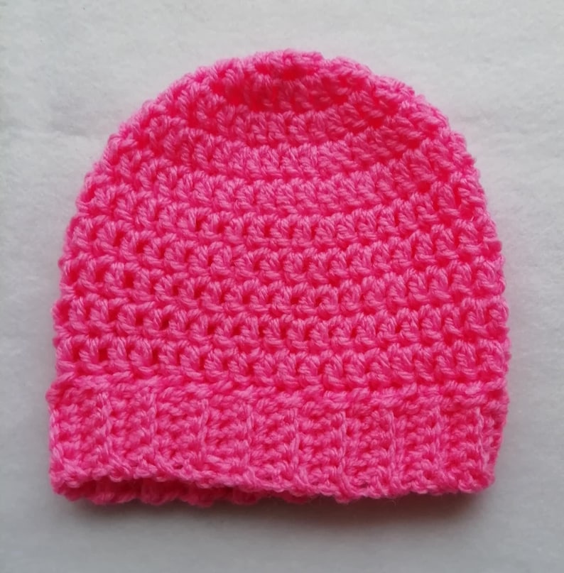 May include: A bright pink, handmade crochet beanie hat. The hat is made with a textured stitch and features a ribbed brim. The hat is a solid color and appears to be made of soft yarn.