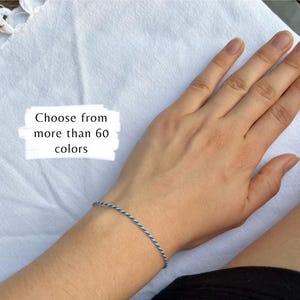 May include: A blue and white twisted cord bracelet is worn on a wrist. The image includes the text, "Choose from more than 60 colours."