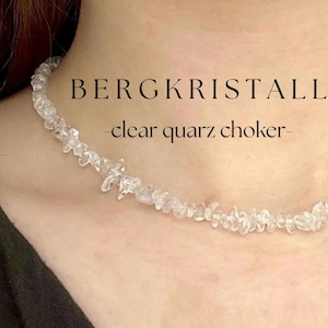 Puede incluir: Un collar gargantilla de cuarzo transparente. El collar está hecho de pequeñas piedras de cuarzo transparente de forma irregular ensartadas. El texto "BERGKRISTALL - clear quartz choker-" se muestra encima del collar.