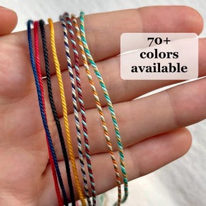 May include: A collection of thin, twisted cord strings in various solid and multi-colored patterns, including blue, red, black, yellow, and teal combinations. A white rectangular overlay displays the text 70+ colors available.