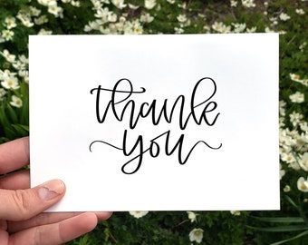 Puede incluir: Una tarjeta blanca con las palabras "gracias" escritas en cursiva negra.