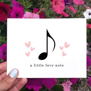 May include: A white card with a black musical note and pink hearts. The text "a little love note" is printed below the note.