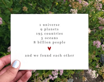 May include: A white card with black text listing: 1 universe, 9 planets, 195 countries, 5 oceans, 8 billion people, and a red heart. The text at the bottom reads: and we found each other.