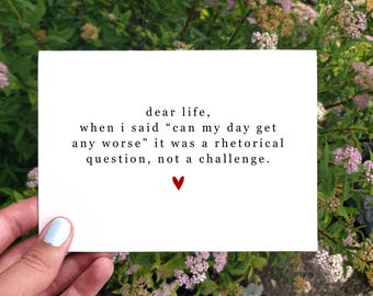 May include: A white card with black text that reads "dear life, when i said "can my day get any worse" it was a rhetorical question, not a challenge." A small red heart is at the bottom of the card.