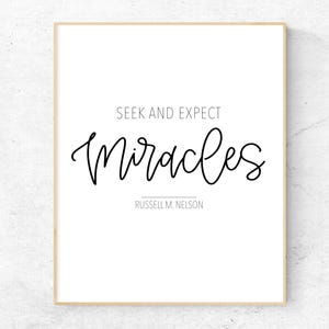 May include: A framed print featuring the words "Seek and Expect Miracles" in black script. The print also includes the name "Russell M. Nelson". The frame is light brown, and the background is white.