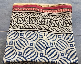 May include: A white cotton fabric with a blue and white geometric pattern. The fabric has a red, black, and white border.