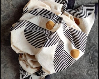 May include: A white fabric with black and gold geometric patterns. The fabric is folded and has a textured surface.