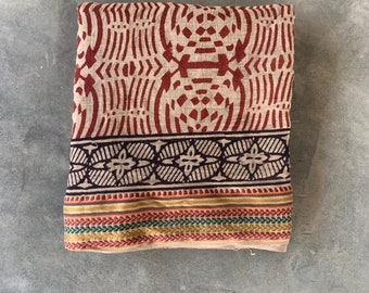 May include: A beige cotton throw blanket with a red and black geometric pattern. The blanket has a border with a smaller geometric pattern in brown, black, and yellow.