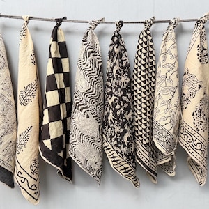 Puede incluir: Diez paños de tela cuadrados con varios estampados negros sobre fondo crema, incluyendo formas geométricas, motivos animales y diseños botánicos, cada uno atado por la esquina superior a una cuerda horizontal para su exhibición.