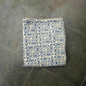 May include: A blue and white patterned fabric with a geometric design of overlapping circles. The fabric is folded in half and lying on a gray surface.