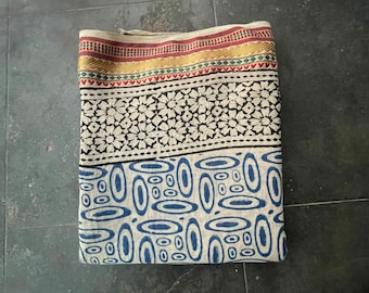 May include: A folded fabric with a white background and blue, black, red, and gold patterns. The fabric has a border with a geometric design.