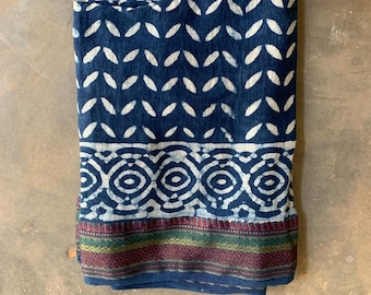 May include: A blue cotton fabric with a white leaf pattern and a white geometric border. The fabric has a red, green, and gold trim.