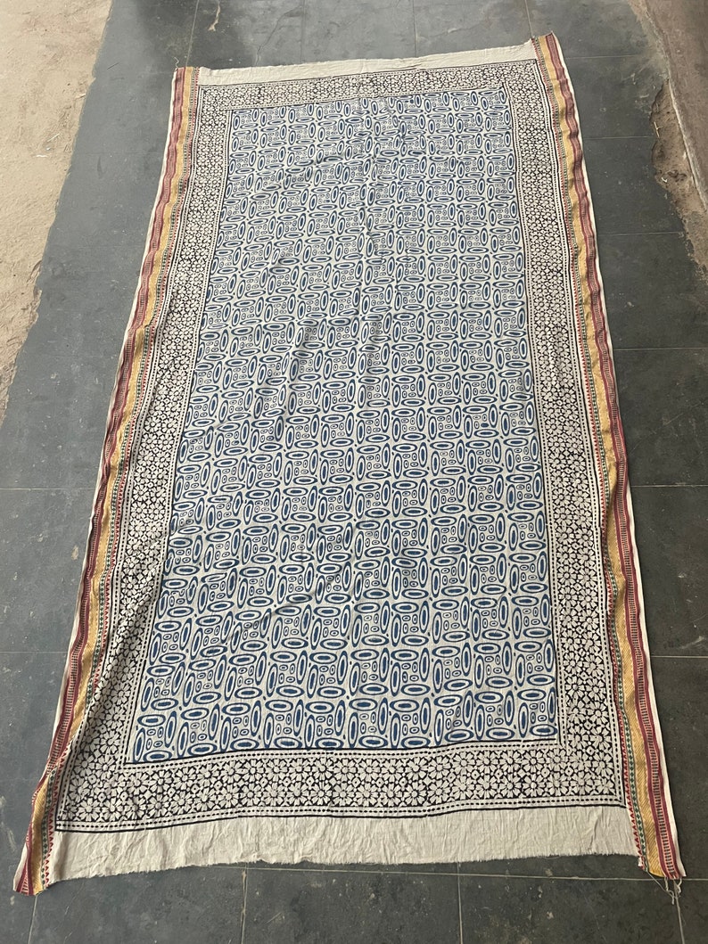 May include: A white cotton fabric with a blue and black geometric pattern. The fabric has a border with a floral design in black and white.