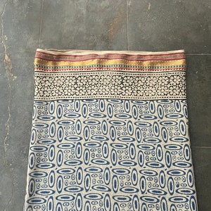 May include: A cream-colored fabric with a blue and white geometric pattern. The fabric has a gold, red, and green border.