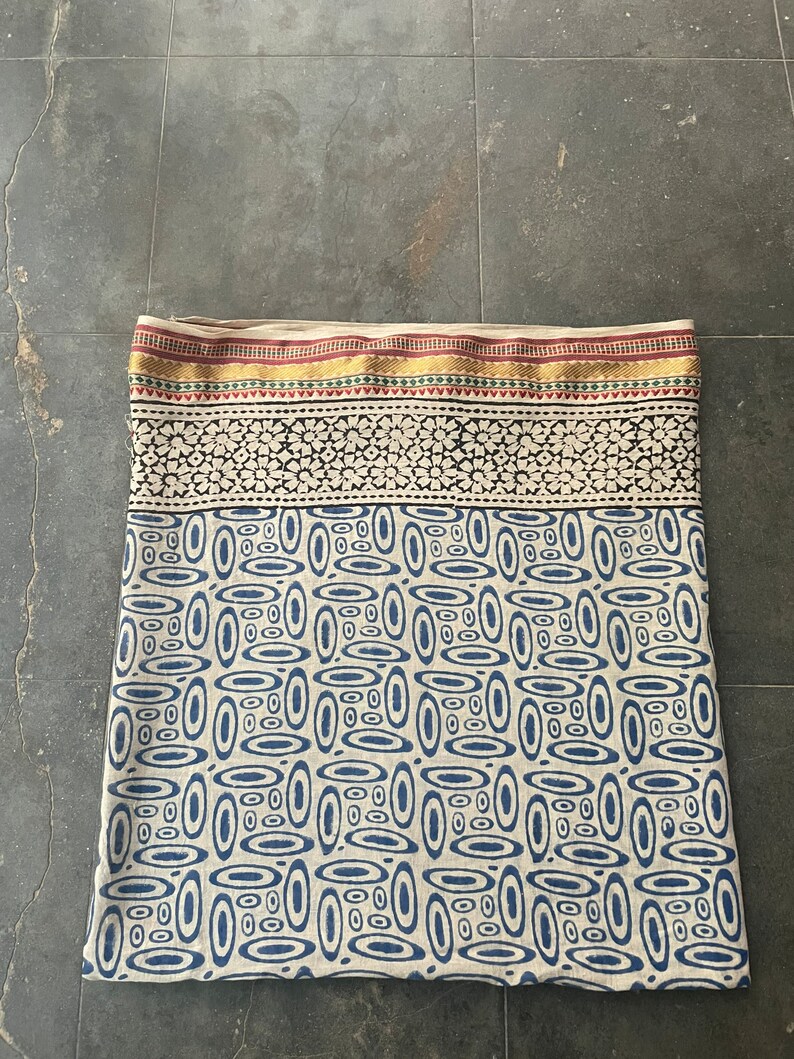 May include: A cream-colored fabric with a blue and white geometric pattern. The fabric has a gold, red, and green border.