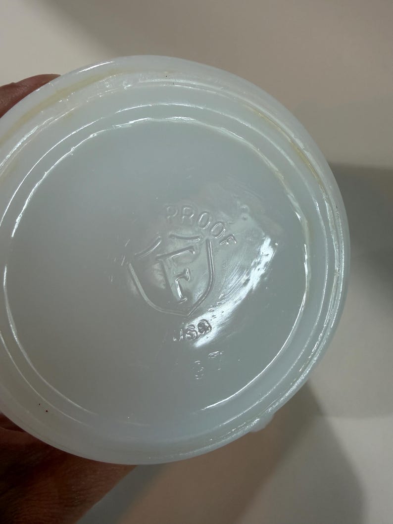 Może przedstawiać: Okrągła, p&oacute;łprzezroczysta podstawa z białego szkła mlecznego z wytłoczonym logo na środku. Logo składa się z tarczy zawierającej literę F, z wygiętym łukowato słowem PROOF powyżej oraz literami USA i liczbą 37 umieszczonymi poniżej.