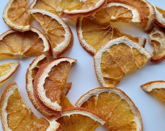 May include: Dried orange slices, a popular ingredient for crafting and decorating, are arranged on a white surface. The slices are a vibrant orange colour and have a slightly translucent appearance.