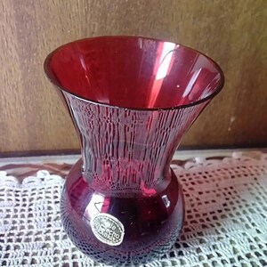 May include: A deep red glass vase with a textured surface and a round base. The vase has a label that reads "Made in Czechoslovakia".