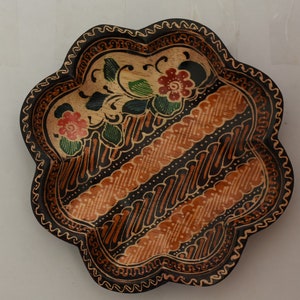 May include: A wooden serving dish with a black and brown batik pattern. The dish is decorated with red, green and yellow flowers.