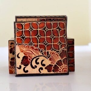 Op de afbeelding: Houten doosjesset met een decoratief batikontwerp. De dozen hebben een warm kleurenpalet van bruin, zwart en beige. Het ontwerp bevat bloemen en geometrische patronen.