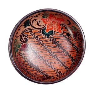 Pode incluir: Uma tigela de madeira redonda com um design batik marrom, preto e vermelho. A tigela tem um padrão floral com folhas verdes e uma flor vermelha.