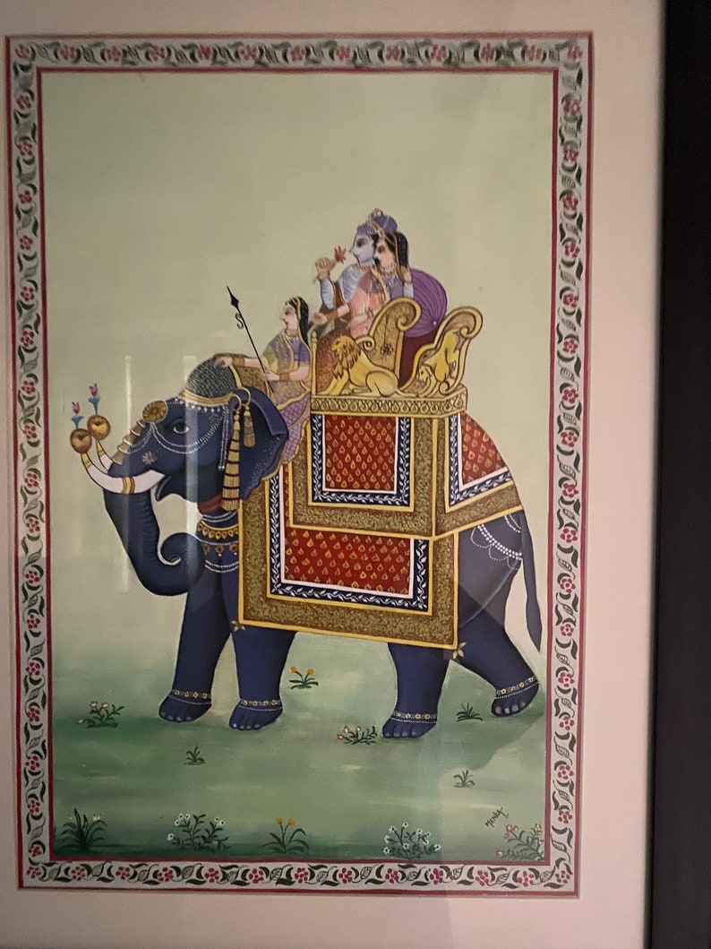 May include: A traditional Indian painting depicting a blue elephant carrying a decorated howdah with four figures inside. The elephant is adorned with gold and red embellishments, and the howdah is decorated with intricate patterns. The painting is set against a light green background with a floral border.
