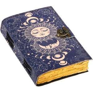 Op de afbeelding: Een blauw lederen gebonden dagboek met een zon- en maandesign. De omslag heeft een gedetailleerde illustratie van een zon met een gezicht en een wassende maan. Het dagboek heeft een sluiting van messing.