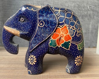 May include: A hand-painted wooden elephant figurine with blue, orange, green and yellow floral designs. The elephant is standing on a wooden surface.