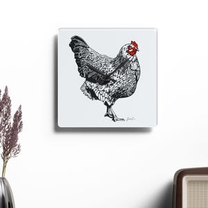 May include: A square wall clock featuring a detailed black and white ink-style illustration of a chicken with a bright red comb and wattle. The clock face is white with black hands and a small signature in the bottom right corner of the illustration.