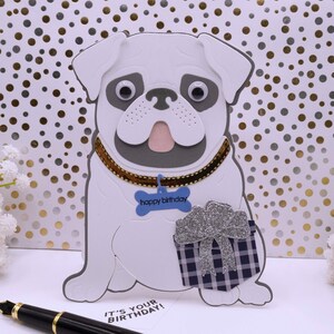 May include: A white pug dog birthday card with a blue bone that says "happy birthday" and a silver glitter gift box with a blue and white plaid pattern. The card says "it's your birthday!" at the bottom.