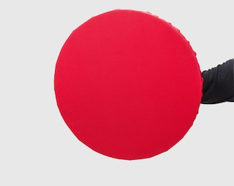 May include: A circular, vibrant red fabric cover with a smooth, solid-coloured surface and a gathered, elasticised edge. The material appears taut across the round frame, creating a clean, uniform appearance with no visible patterns or textures.