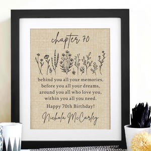 May include: A framed print on a tan burlap-textured background featuring black line art of wildflowers and the text: chapter 70, behind you all your memories, before you all your dreams, around you all who love you, within you all you need. Happy 70th Birthday! Nichola McCarley.