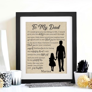May include: A framed print with a burlap background and black silhouettes of a father and daughter. The text reads "To My Dad" and includes a heartfelt message about the importance of a father's love and support. The print is signed "Marina".