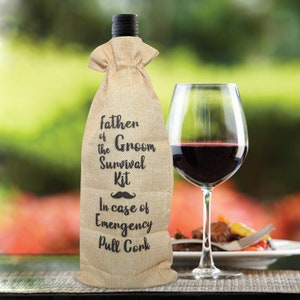 May include: A burlap wine bottle bag with the text "Father of the Groom Survival Kit" and a mustache graphic. A glass of red wine sits next to the bottle, with a blurred outdoor background.