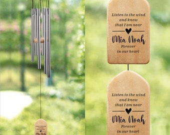 May include: A wooden wind chime with a beige finish and a heart-shaped cutout. The chime features the text "Listen to the wind and know that I am near Mia Noah Forever in our heart".