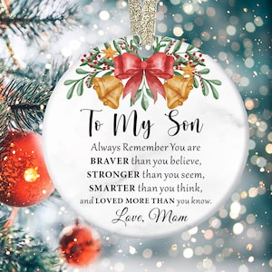 May include: White marble Christmas ornament with a red bow and gold bells. The ornament has the text "To My Son" and a message about being brave, strong, smart, and loved. The ornament is signed "Love, Mom".