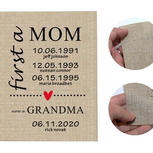 May include: A rectangular burlap canvas print with the words "first a MOM" in black script. Below are dates and names, followed by "now a GRANDMA" and another date and name. A red heart is between the two phrases.