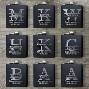 May include: Nine black metal hip flasks with engraved silver lettering. Each flask features a different initial and name, along with the title "Groomsmans" and a date.