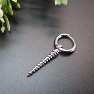 May include: Silver hoop earring with a dangling spiral design. The earring is made of metal and has a polished finish.