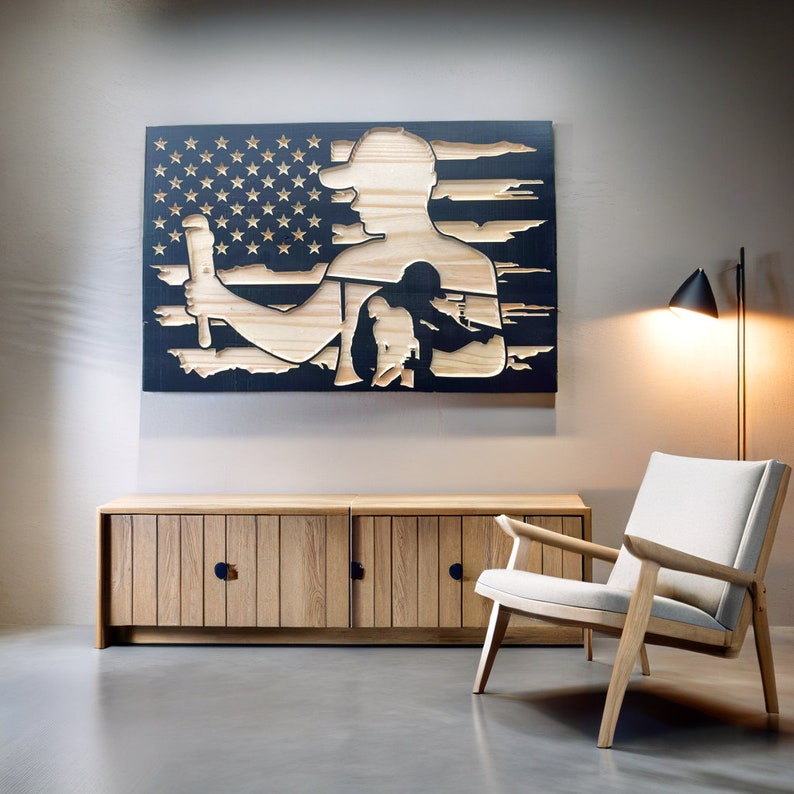 May include: Wooden wall art depicting a silhouette of a person holding a tool, set against a backdrop of the American flag. The artwork is made of light-colored wood and black paint. The piece is mounted above a wooden cabinet.