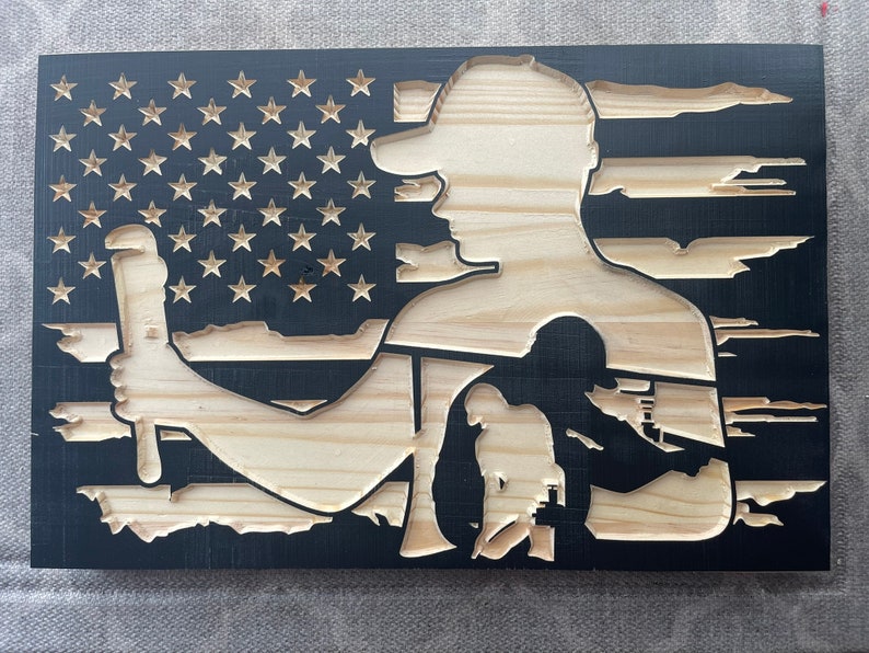 May include: Wooden wall art featuring a carved design of an American flag with a silhouette of a worker holding a wrench. The flag's stars and stripes are visible, with the worker's form in natural wood against a black background.