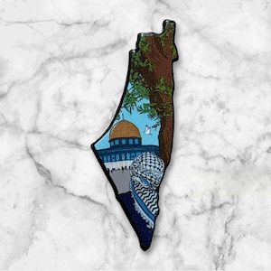Könnte beinhalten: Eine schwarze Metallumrandung des Landes Israel mit einem detaillierten Bild der Felsendom-Moschee in Jerusalem, einem blau-weißen Keffiyeh und einem Baum im Hintergrund.
