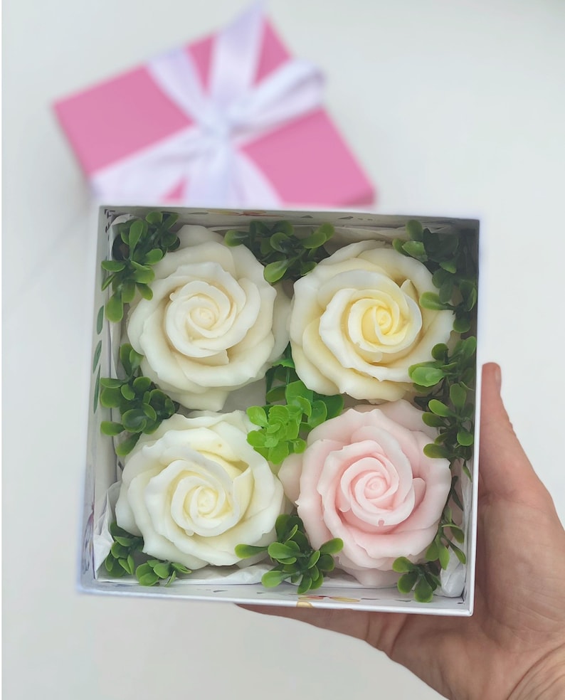 Puede incluir: Una caja de regalo blanca con tapa rosa contiene cuatro rosas de jab&oacute;n. Las rosas son blancas, crema y rosas. Las rosas est&aacute;n rodeadas de hojas verdes.