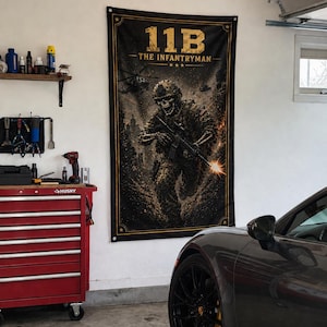 以下が含まれることがあります： 「11B THE INFANTRYMAN」の文字と、ライフルを持った兵士の骸骨のイラストが描かれた、金色の縁取りのある黒いバナー。背景にはヘリコプターが描かれた戦場が描かれています。