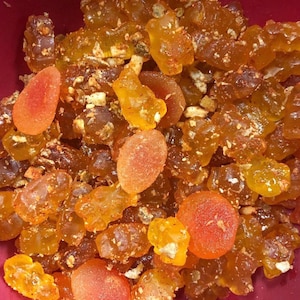 May include: A close-up shot of a mix of candies with a variety of shapes and colors. The candies are primarily amber and orange, with some pieces appearing translucent. Some candies are coated with a fine, light-colored powder.
