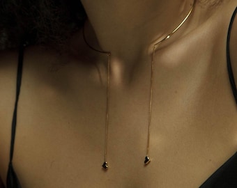 May include: A gold choker necklace with two long chains that end in small heart-shaped charms.