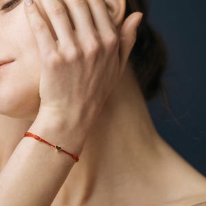 Op de afbeelding: Een rood koord armbandje met een klein gouden hartje.